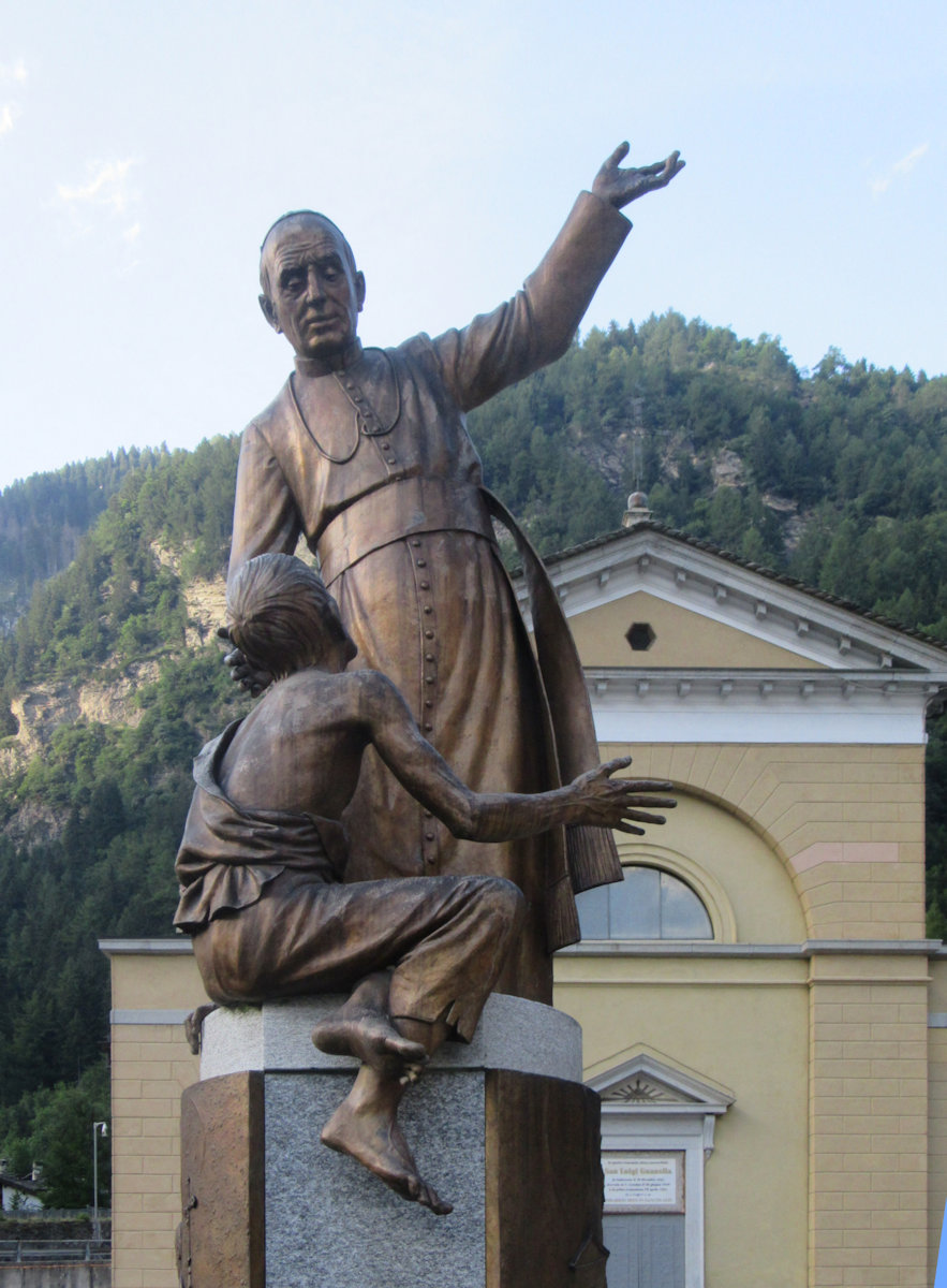 Alfredo Vismara: Denkmal,Inschrift: „Brot und Paradies”, 2008, vor der Kirche in Campodolcino, in der Aloisius getauft wurde