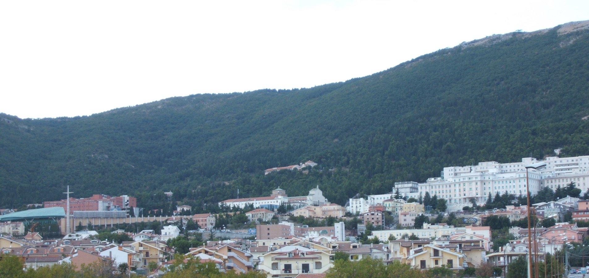 Der Gesamtkomplex von San Giovanni Rotondo aus gesehen: links die neue Kirche, dahinter die neue Poliklinik, in der Mitte die alte Kirche, in der Padre Pio jetzt aufgebahrt ist, dahinter am Berg das Kapuzinerkloster, rechts die alte Klinik